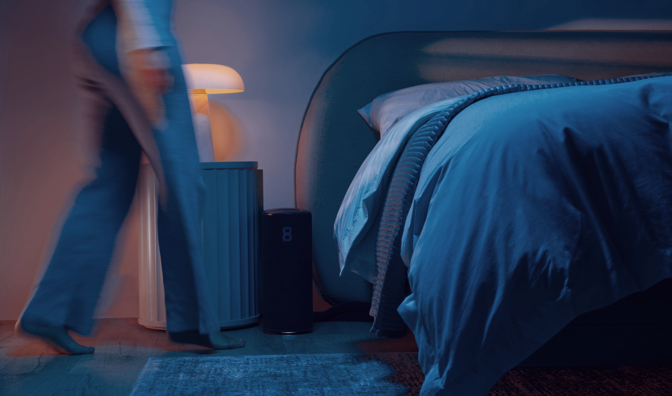 A figure walking towards a bed. The focus of the image is on the Eight Sleep Pod beside the nightstand.